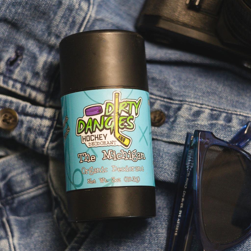 aluminum-free deodorant the michigan scent laying on a pair of jeans with sunglasses and a wallet