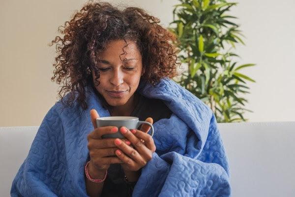 Woman in Blanket with Mug in Hand on Couch Plant
