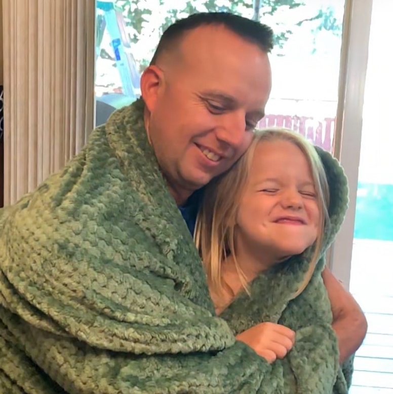 a smiling dad snuggles with his child under a green dutch oven ktis blanket