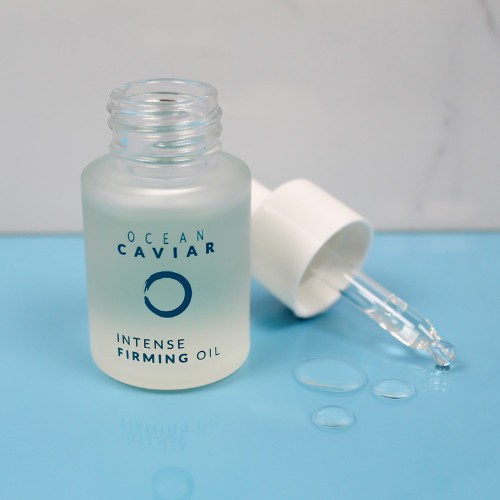 Caviar Firming Oil with its lid off sitting next to the bottle on a half blue, half gray background