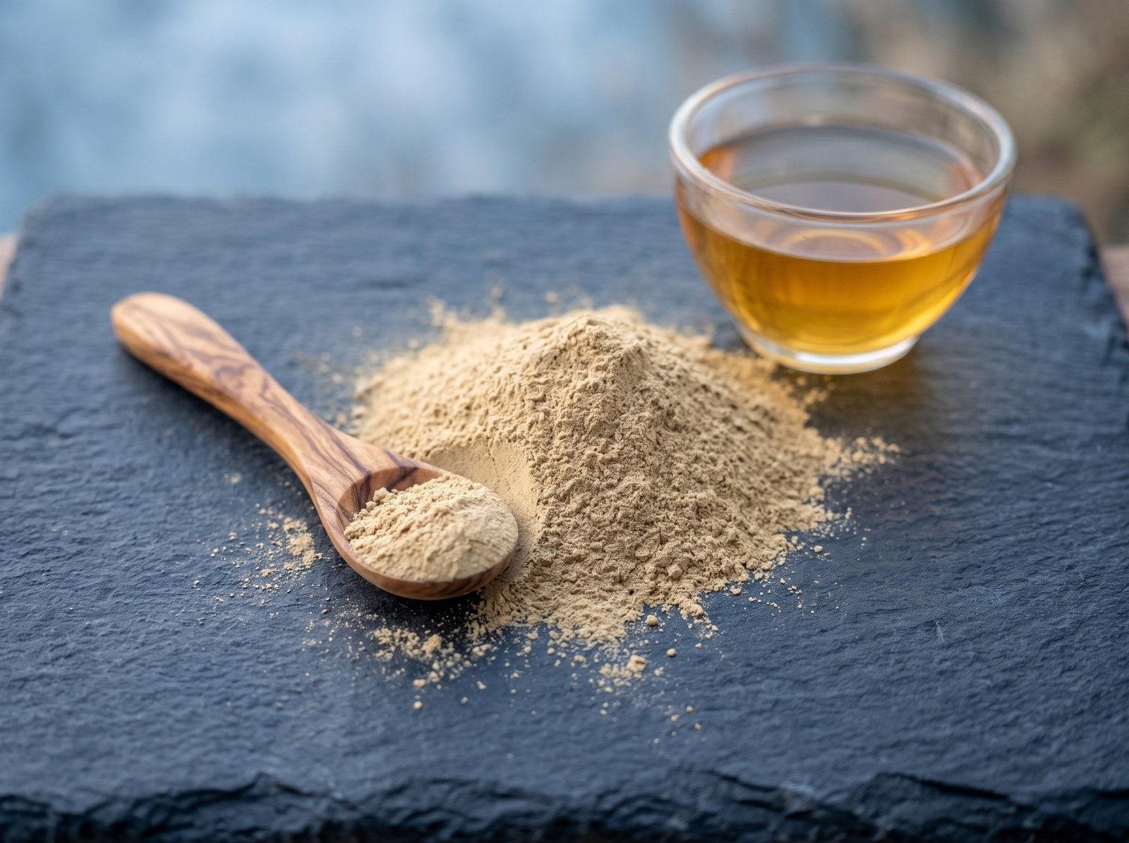 Gynostemma extract powder with a wooden spoon and a glass cup of amber tea on slate