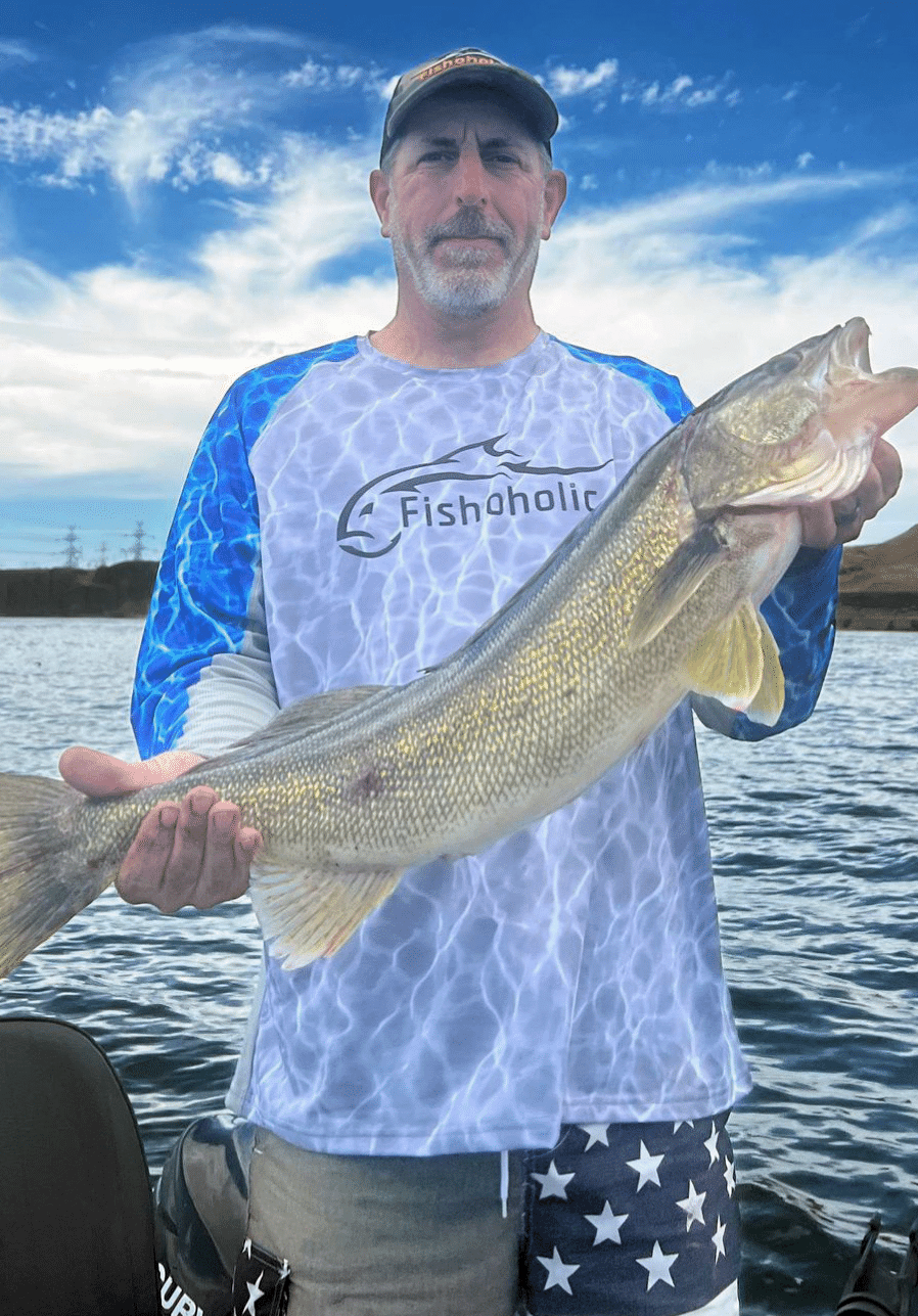 Man holding up large fish wearing Fishoholic fishing shirt on a boat in the water