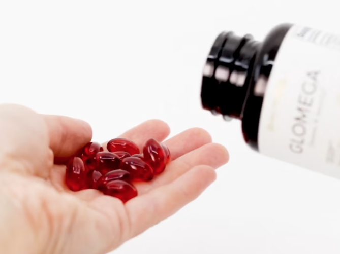 Close-up of a hand pouring Glomega omega-3 soft gel capsules.