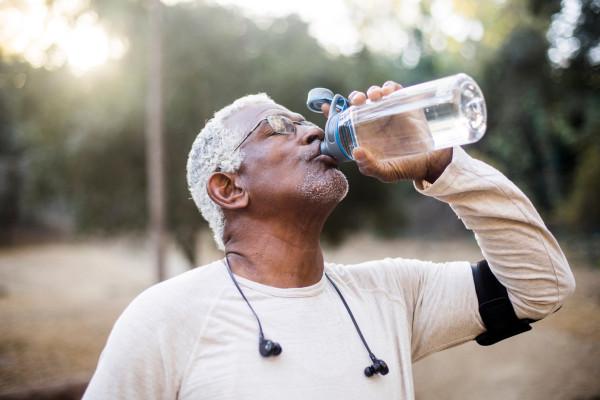 senior man drinking out of a water bottle outside.