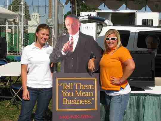 Two women standing next to a standing poster guy