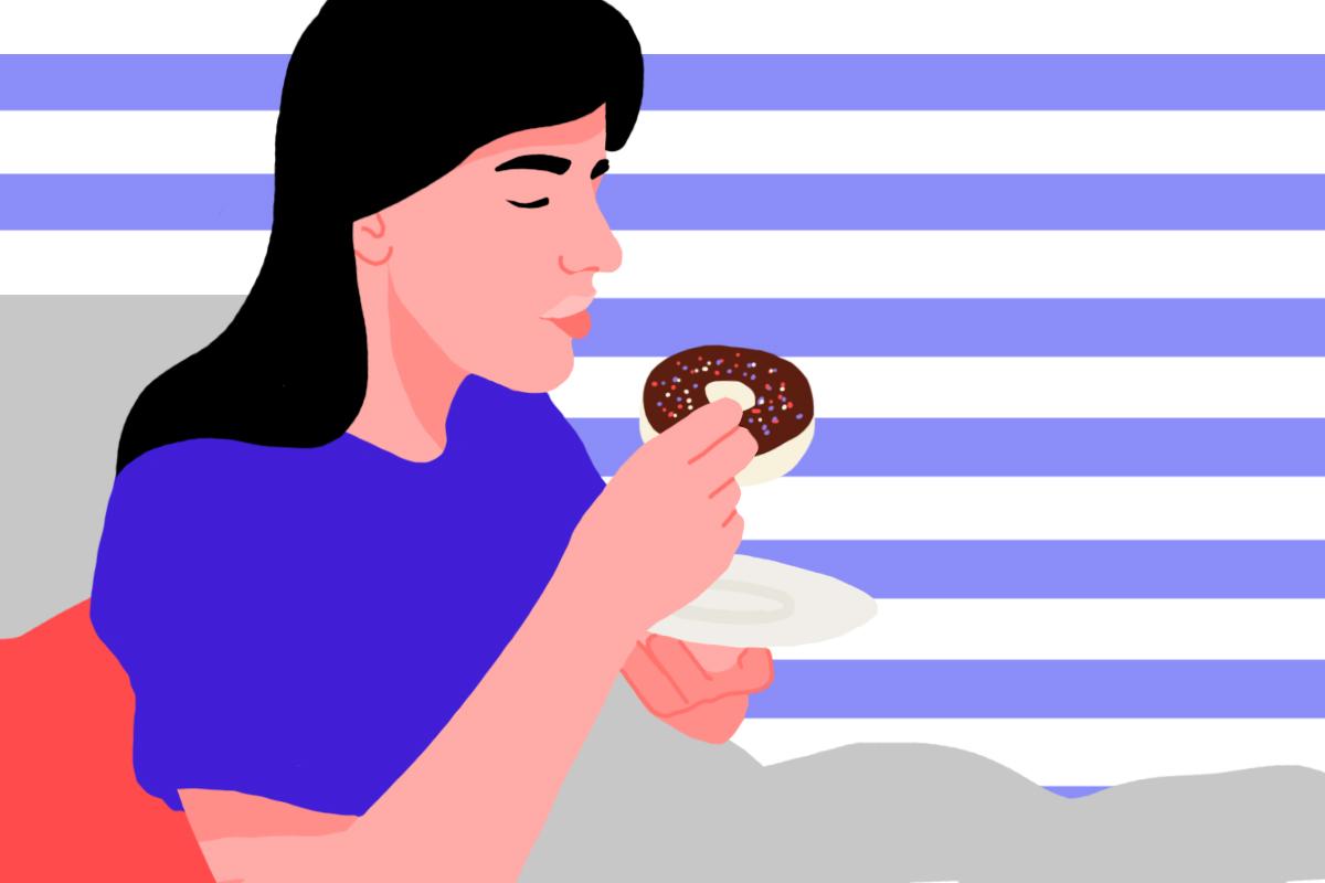 A woman eating a chocolate donut with sprinkles while in bed.