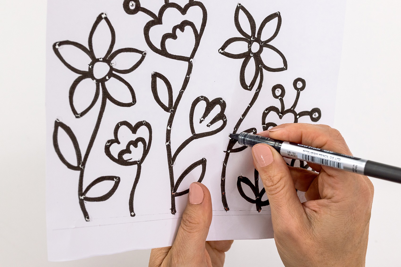 A hand stabs dots in a floral pattern.