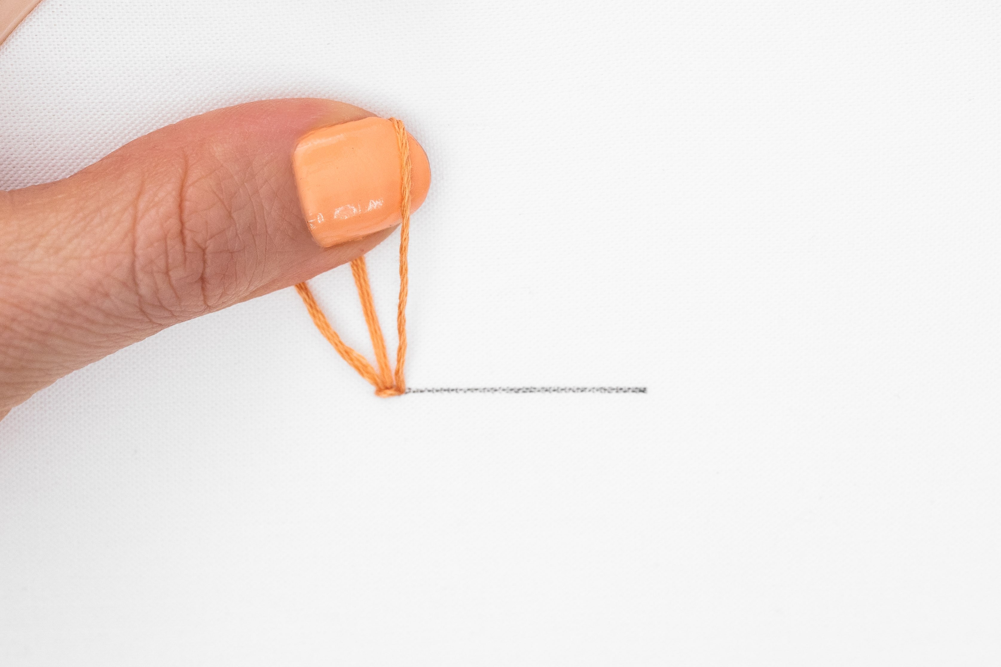 A thumb holds up a loop that has been created from stitching.