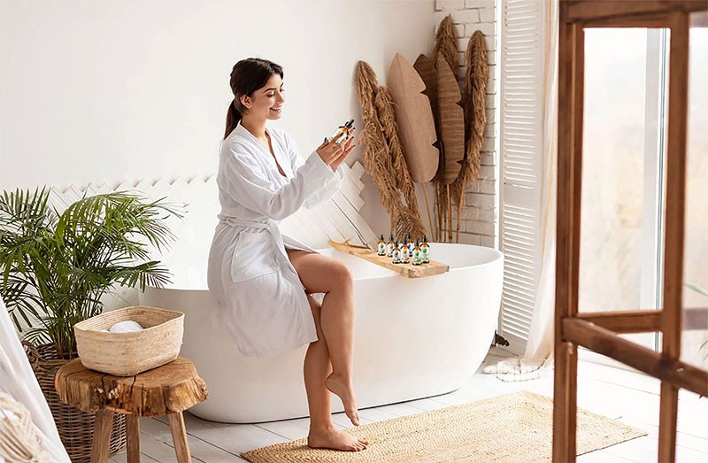 Woman in white robe exploring Bella Terra natural skincare oils in a tranquil, well-lit bathroom setting, with an invitation to shop for authentic natural oil products