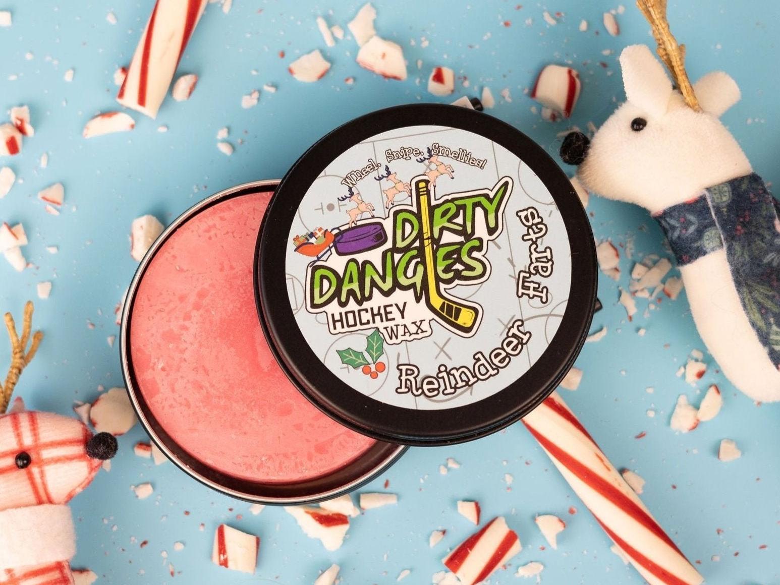 A tin of dirty dangles reindeer farts holiday hockey stick wax on a blue background with candy canes and reindeer
