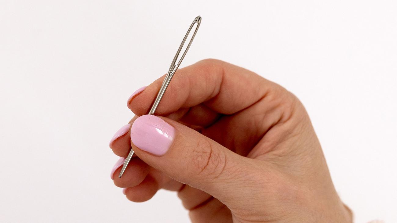 A hand holds a weaving needle.