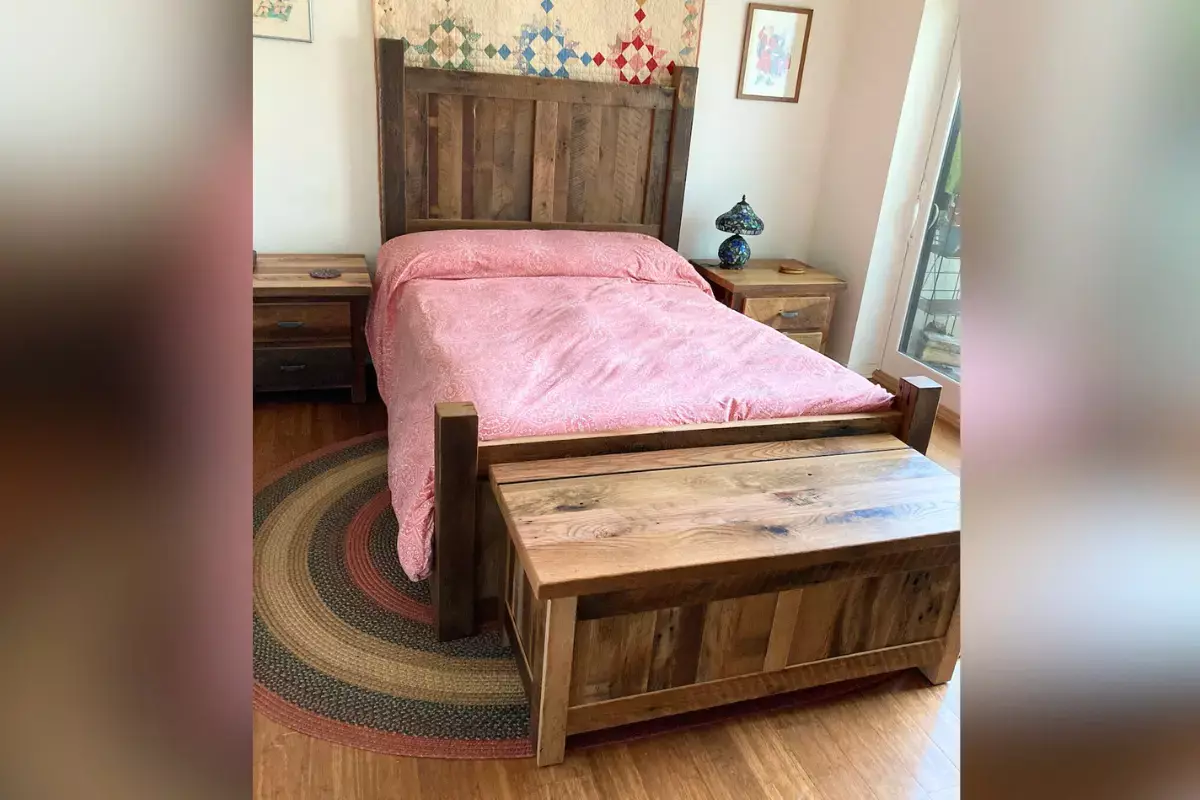 Reclaimed wood bed with low-profile headboard and footboard, matching nightstands, and storage chest in a cozy handcrafted bedroom.