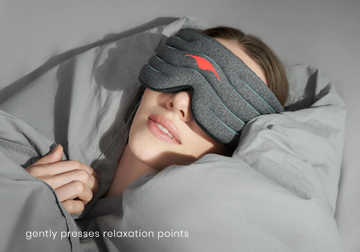A girl lying down wearing a weighted sleep mask surrounded by gray pillows.