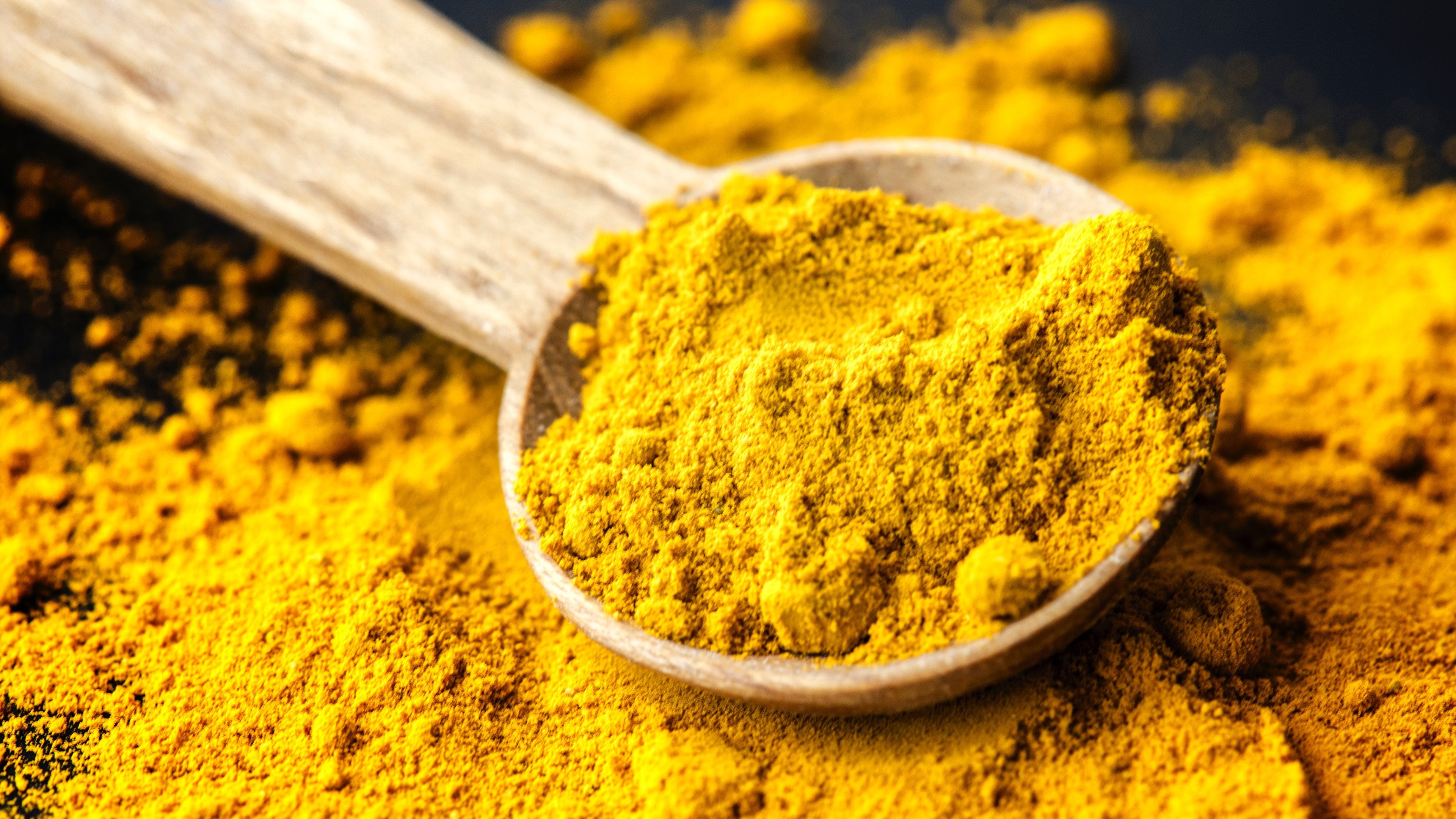 Wooden spoon on a pile of turmeric powder with powder in the spoon.