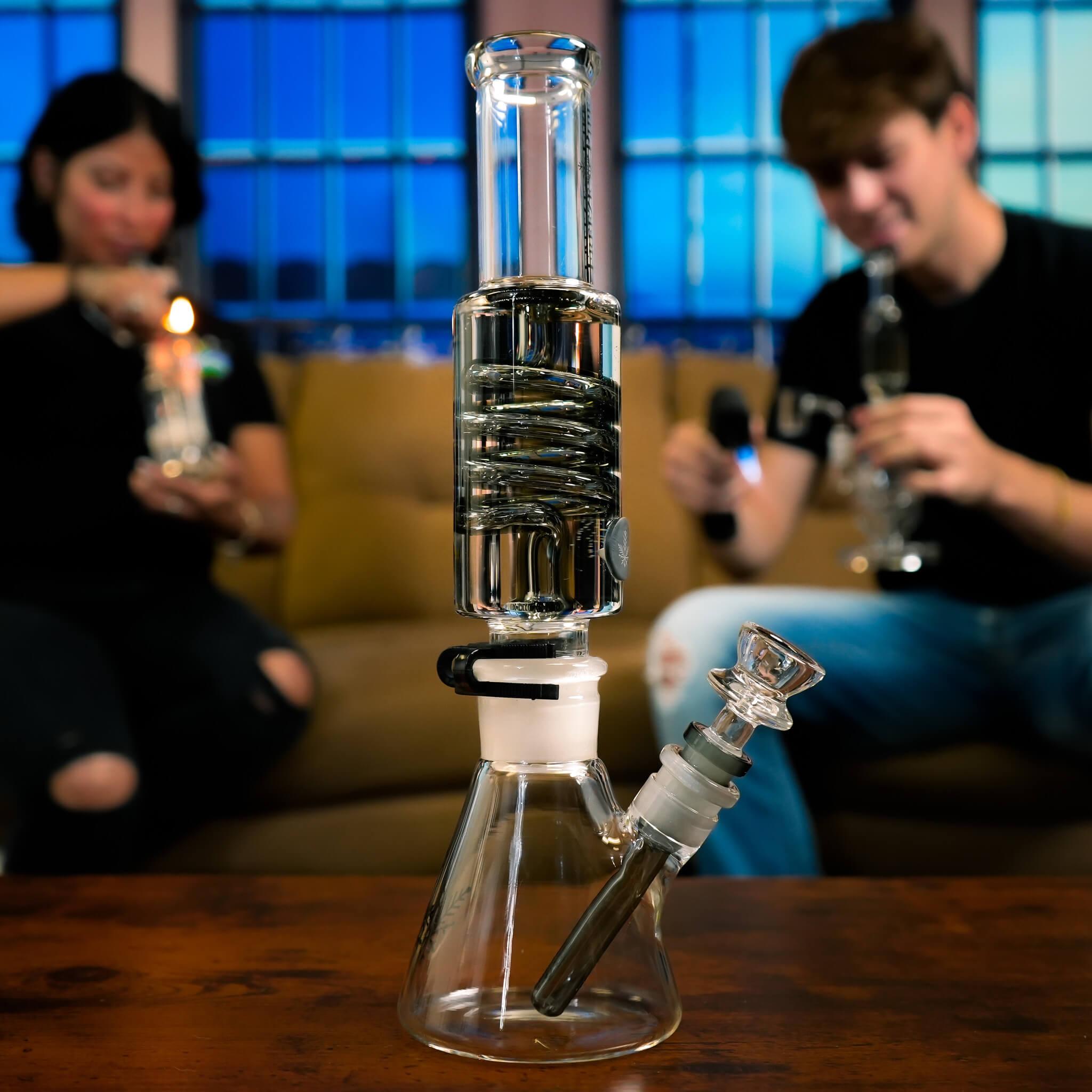 beaker bong on table with people smoking in background