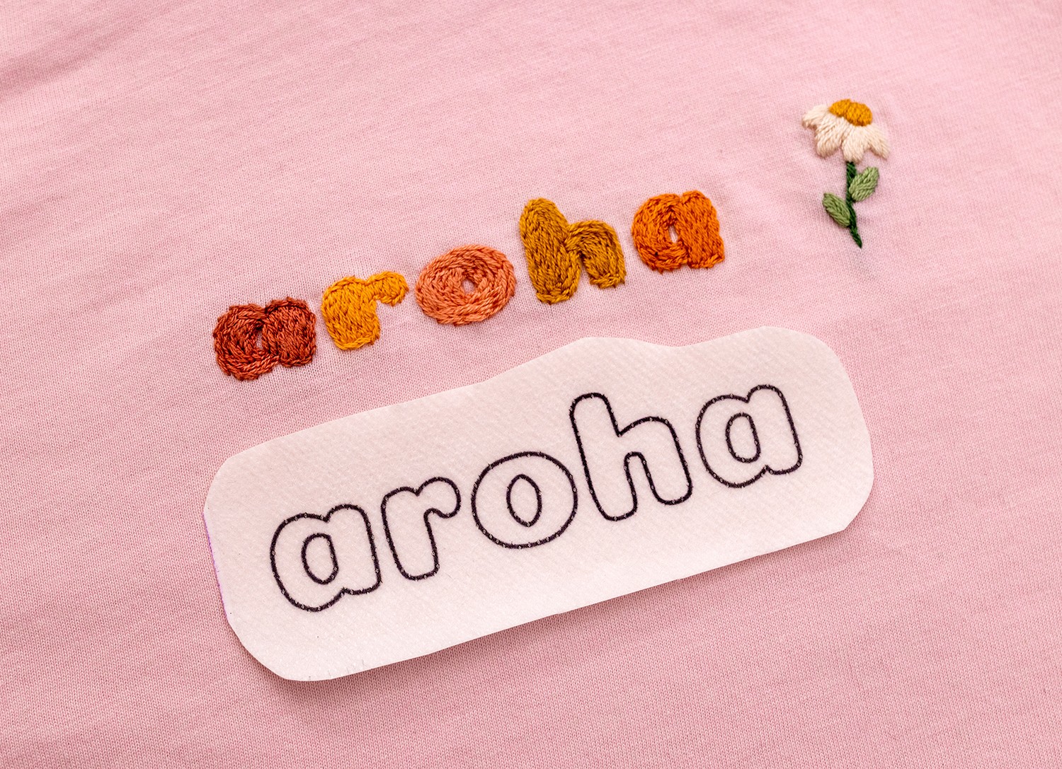 'Aroha' and a flower is stitched on a shirt.