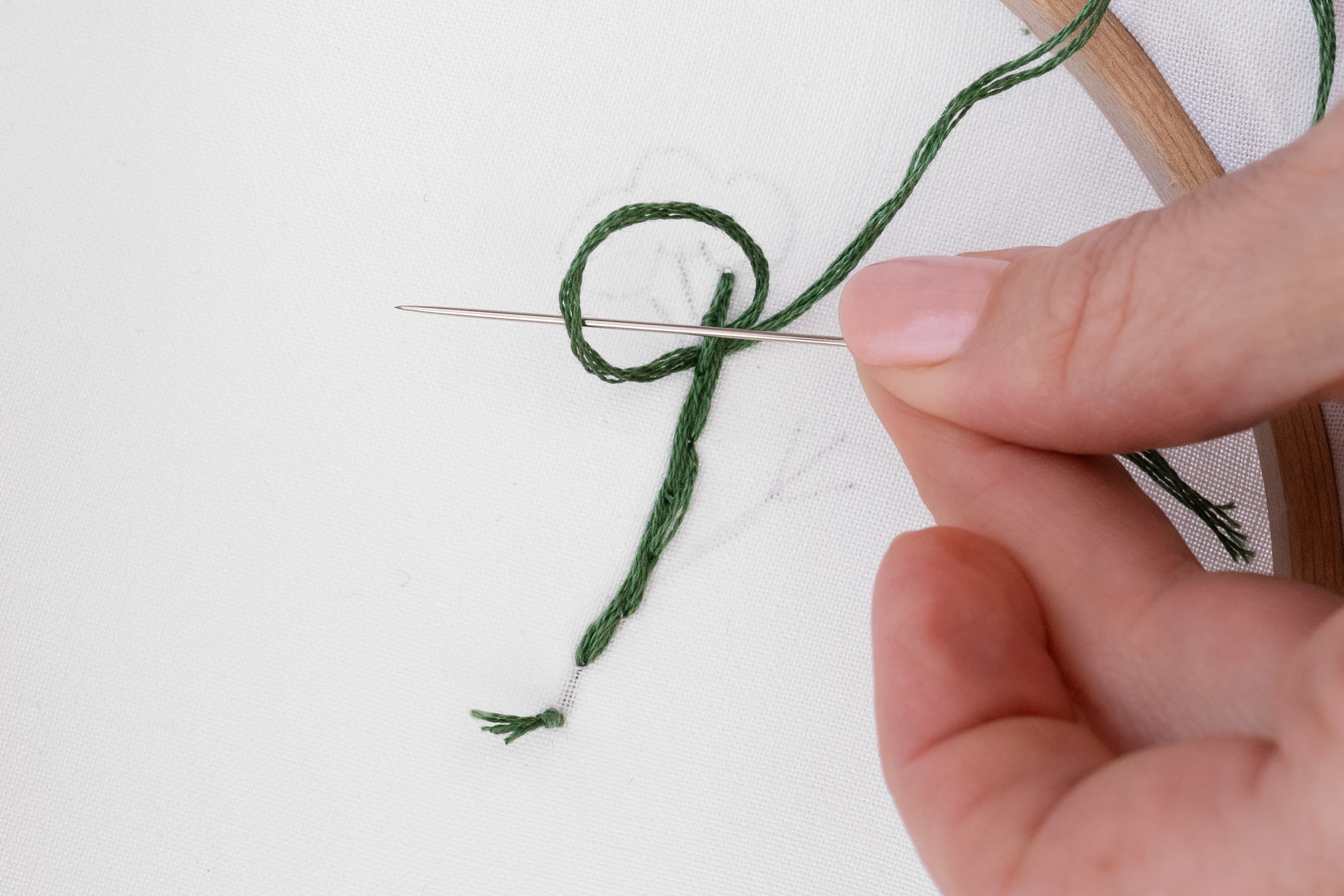 A needle pokes through a loop at the back of the stitching.