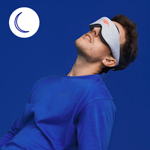A man leaning back while wearing a sleep mask for stomach sleeping with a graphic of a moon on the upper left hand side.