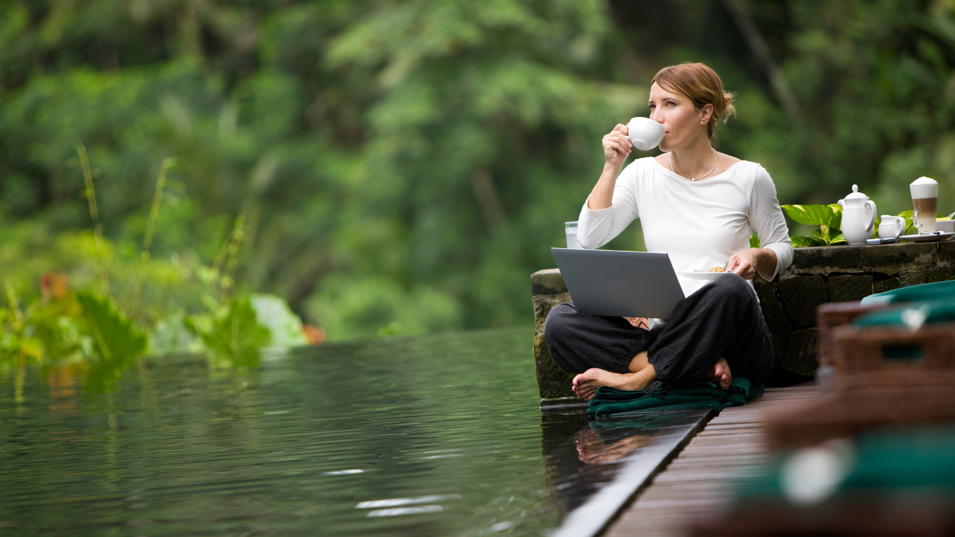 Woman enjoying coffee by the water while working on laptop — Lone Wolf Coffee Co. blog hero image representing reflection, creativity, and connection.