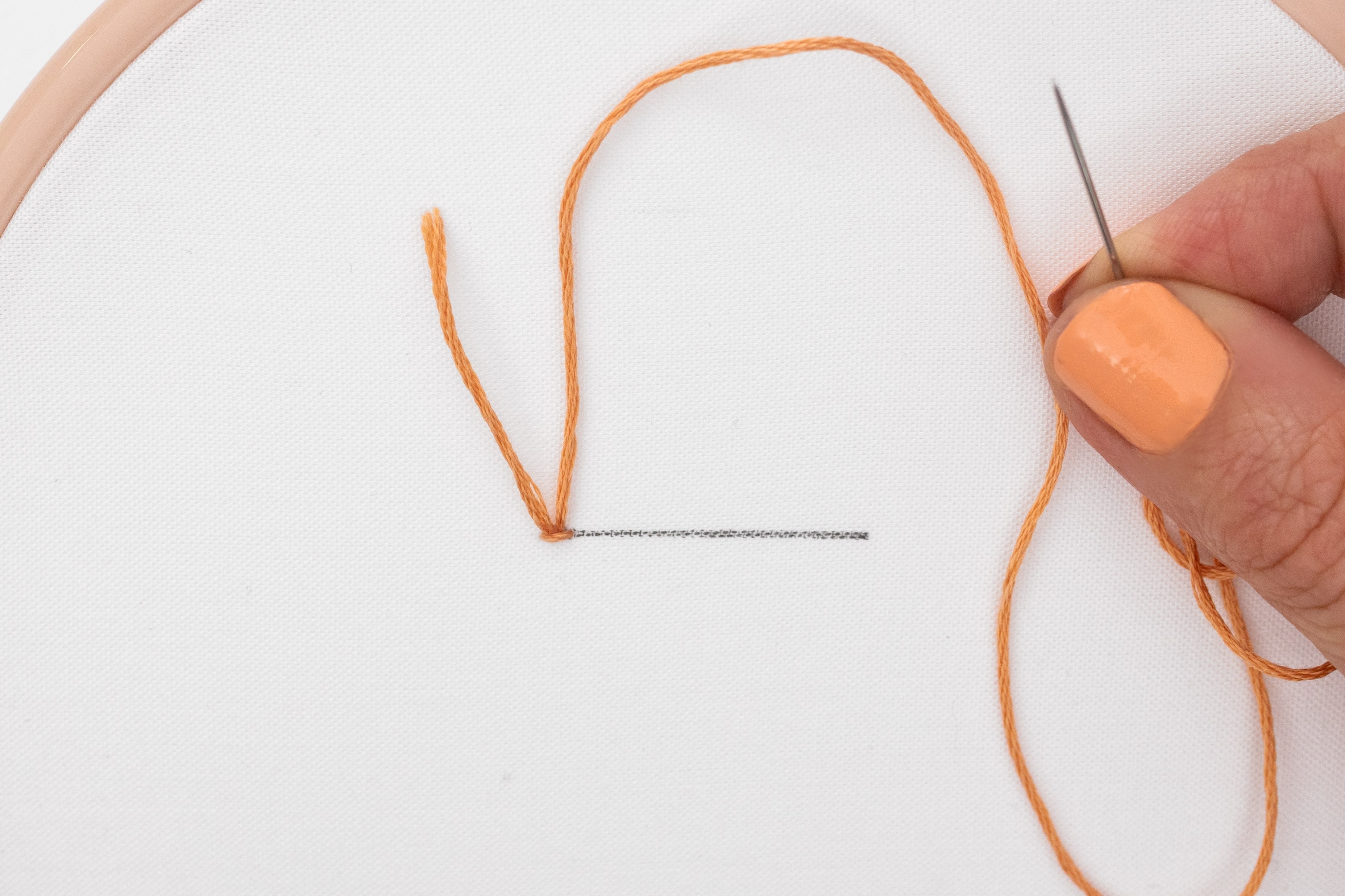 A hand holds up the thread to show that a tidy stitch has been created, holding the tail in place.