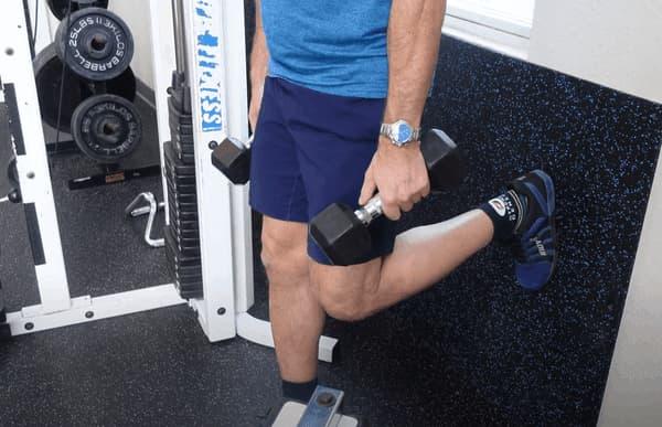 Man In Blue with Shorts Holding Dumbbells in Gym Outside View