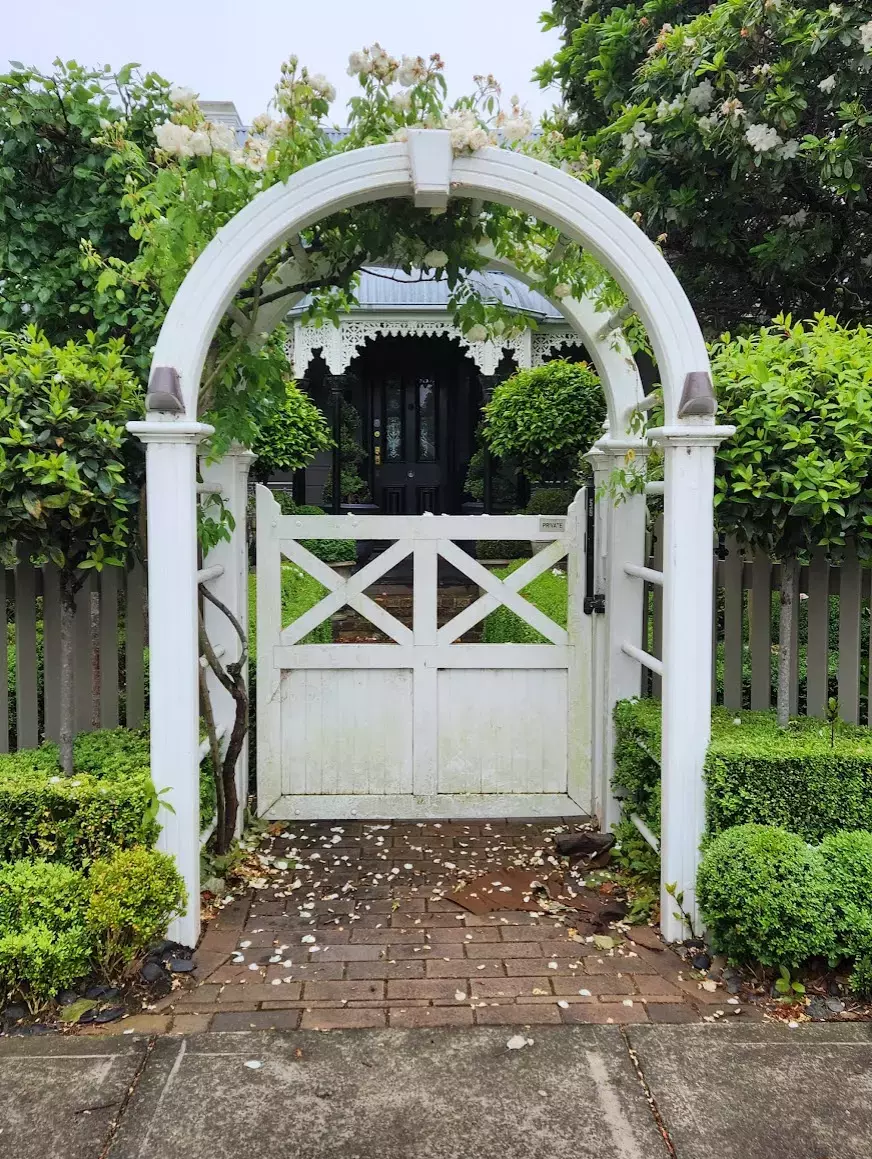 White garden arch with gate framed by greenery and flowering vines.