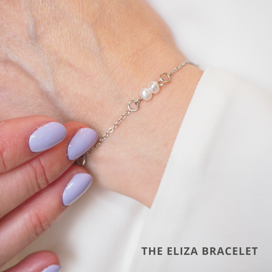 A close up of a woman's wrist with a silver pearl bracelet and purple painted nails.