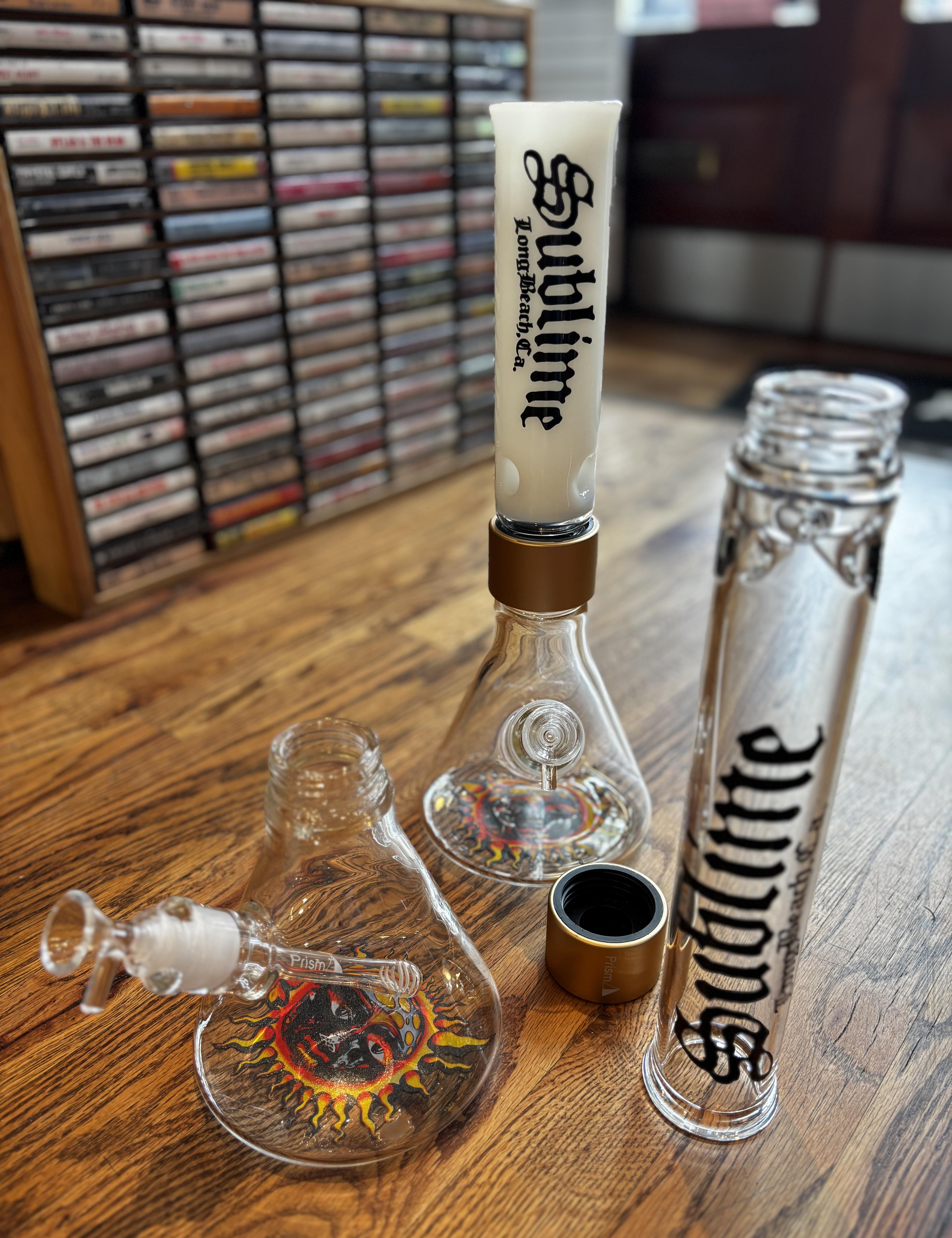 The complete Sublime x Prism official collection featuring clear and white modular glass bongs in both assembled and disassembled states. The gear is displayed on the floor of Creep Records in Philadelphia alongside vintage cassette tapes, showcasing the easy-to-clean threaded Halo Connectors.