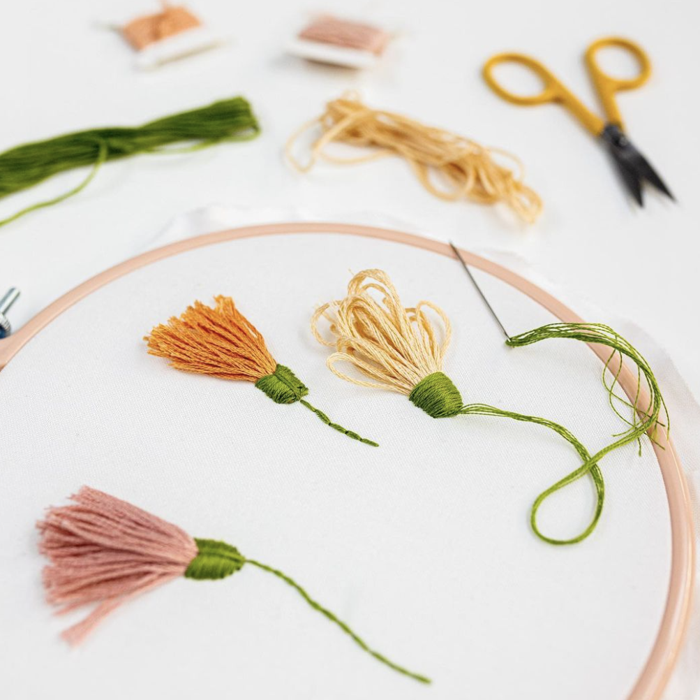 This image shows flowers embroidered onto a Nurge Hoop with DMC Threads and Clever Poppy scissors in the background, available for purchase from the Clever Poppy Shop.