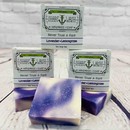 Picture of a box of Shart Wash Natural Handmade Bar Soap Lavender Lemongrass scent sitting on a purple and white bar of soap with a wood background