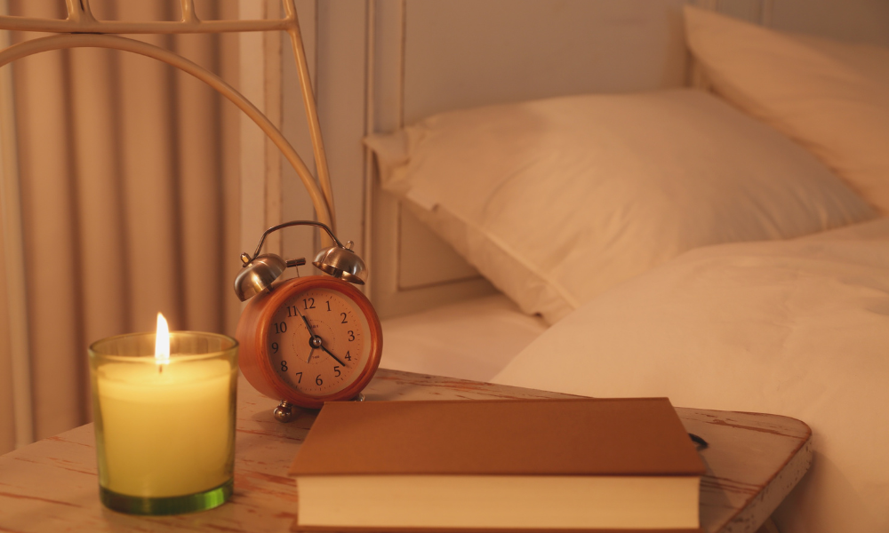 Candle lit book, alarm clock and bed