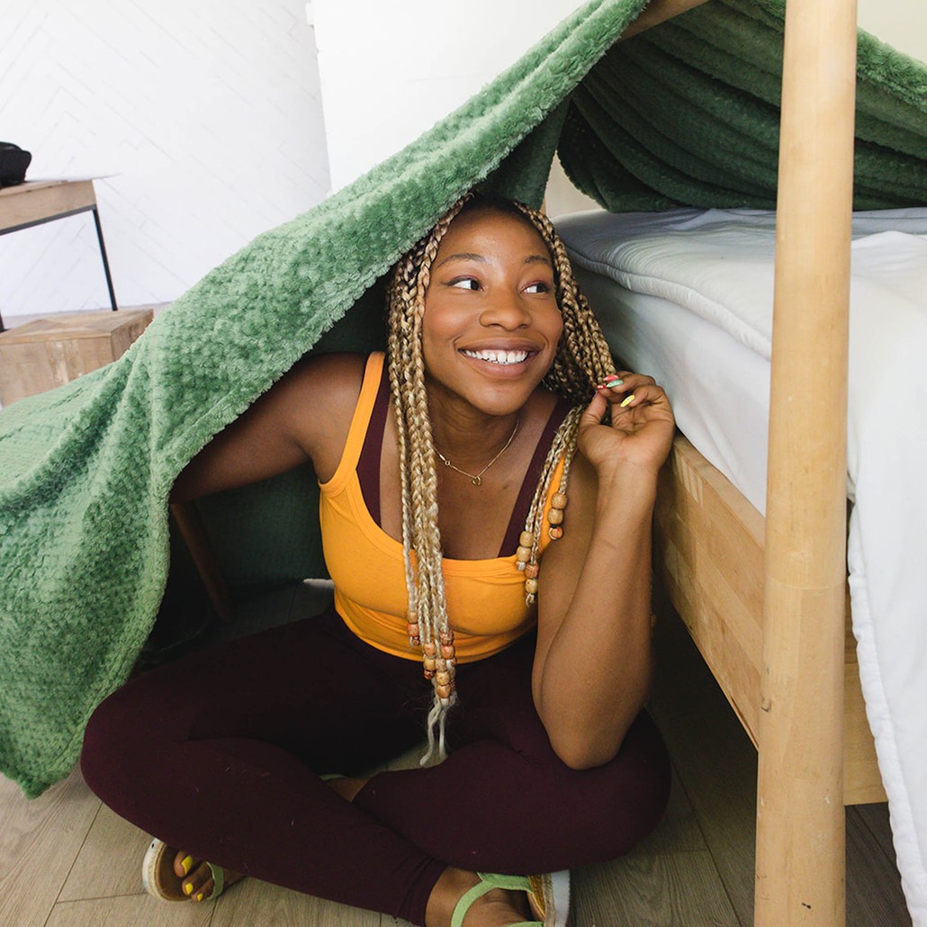 picture of a smiling woman sitting under a green blanket fort