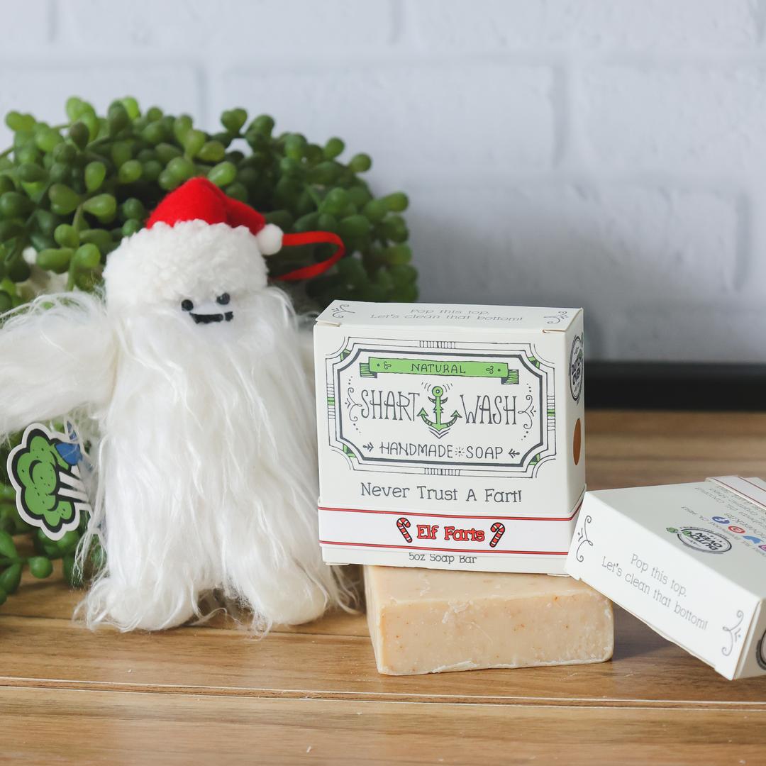 Picture of a box of Shart Wash Natural Handmade Bar Soap, Skid Mark (Charcoal and Aloe) scent sitting on a black and white bar of soap with a wood background