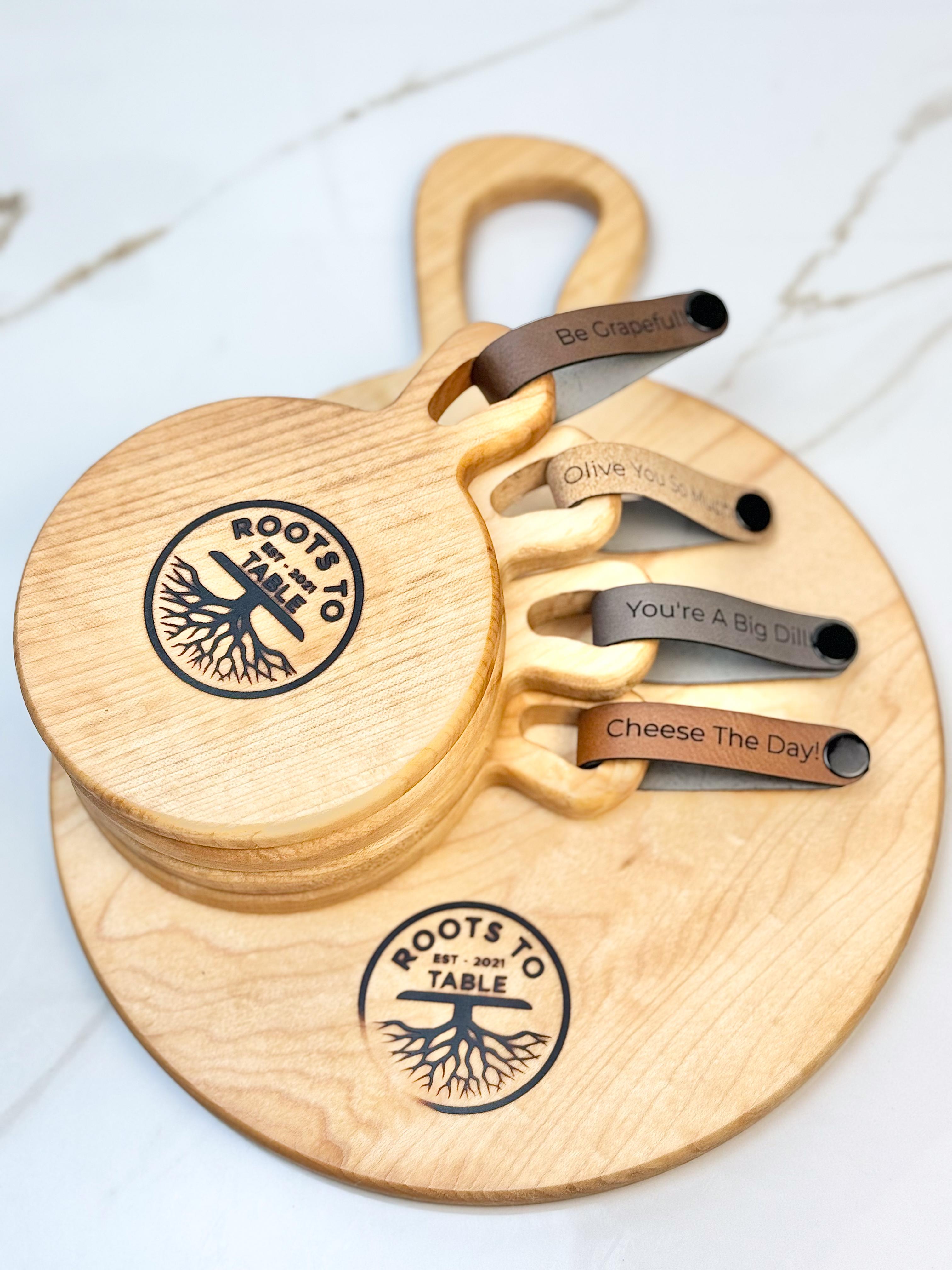 A small round maple charcuterie board with handle and 4 smaller accompanying individual maple rounds with vegan pun tags