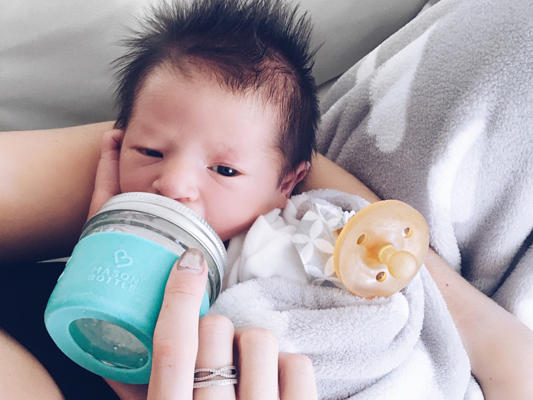 hand holding non-toxic baby bottle with cooler full of breastmilk in background