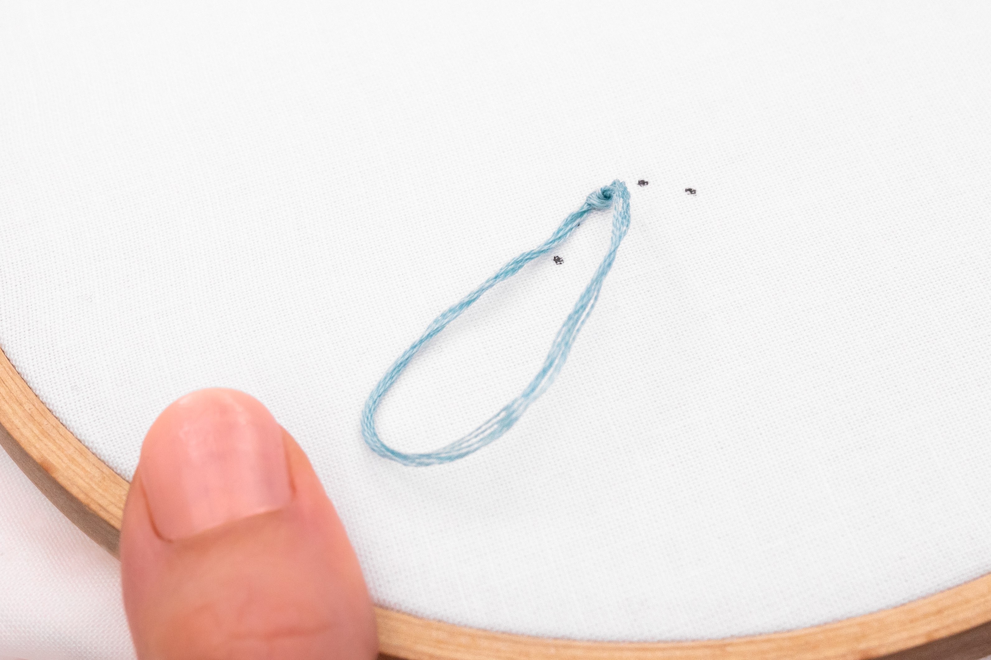 A loop of thread is being pulled into a knot.