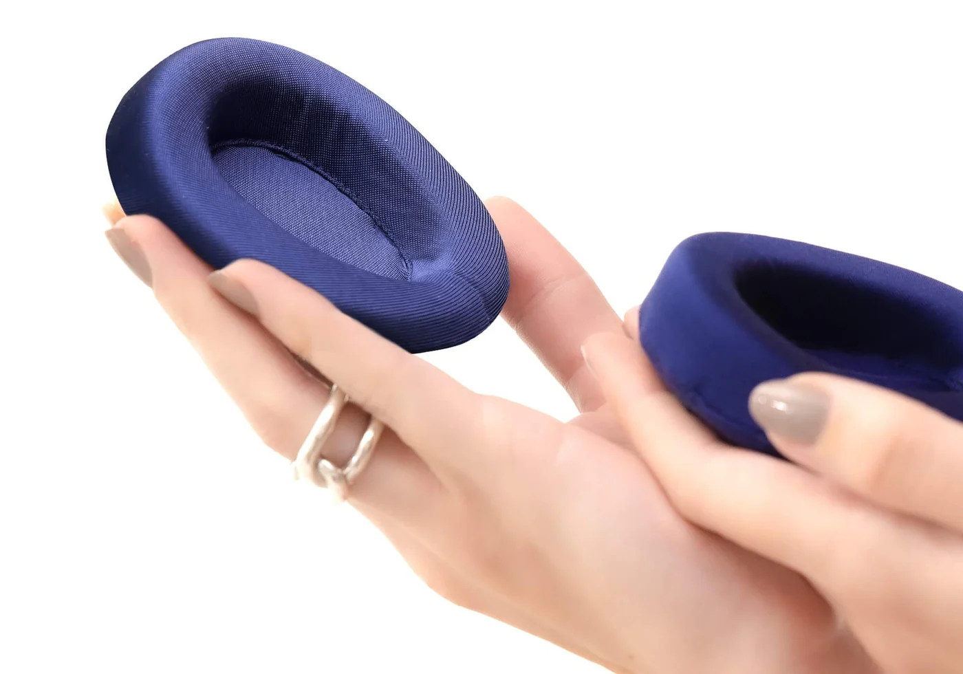 Hands holding 2 blue convex eye cups of a silk sleep mask.