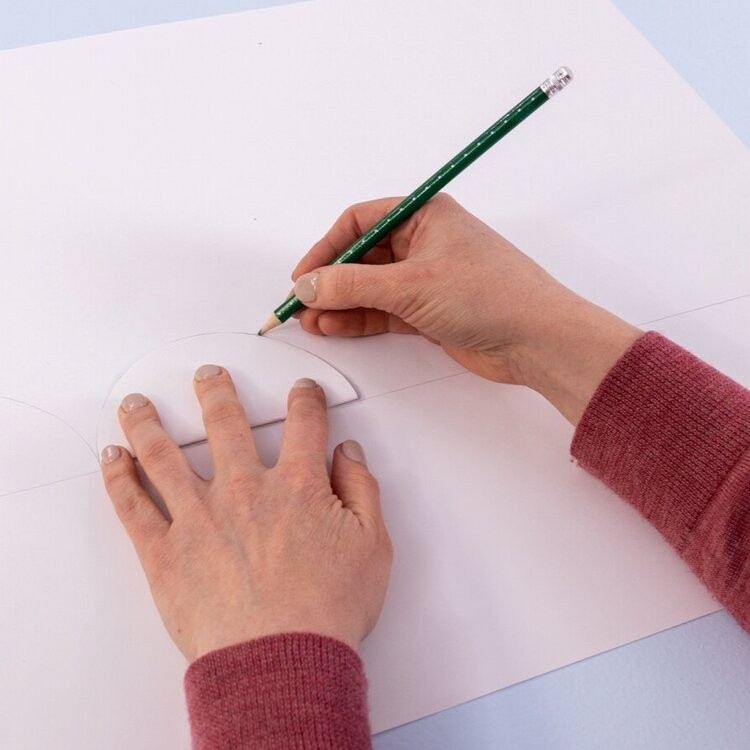 A hand draws around a semi circle with a pencil.