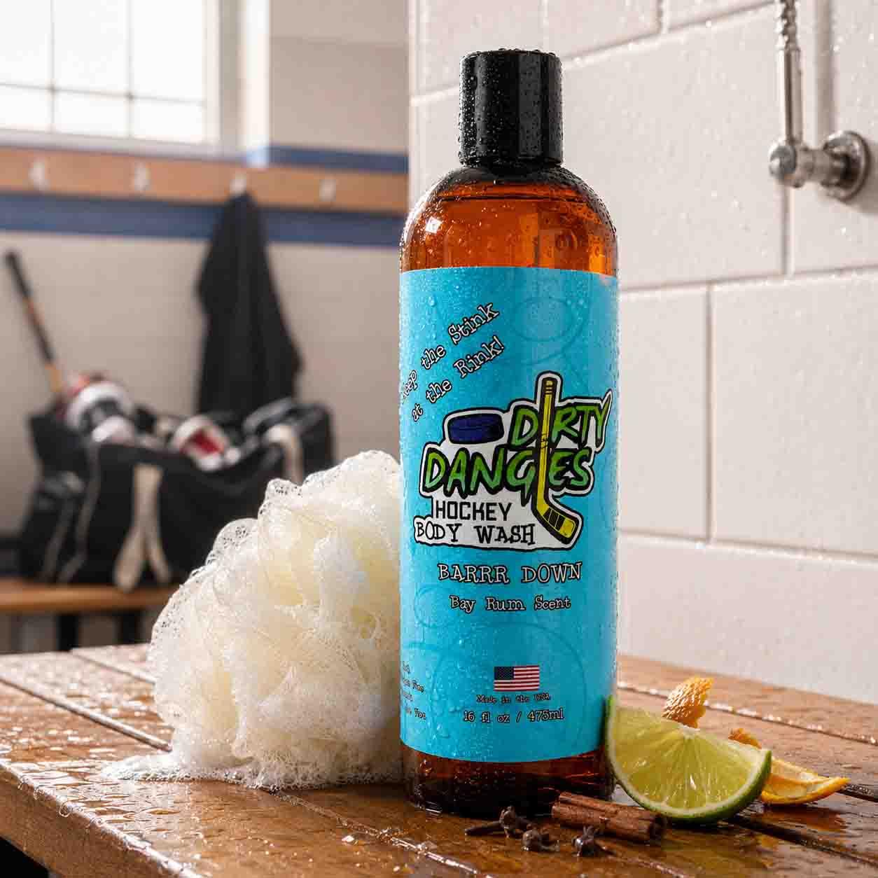 bay rum hockey body wash on a wooden bench inside a hockey locker room with orange peel, lime, spices and a white loofah.
