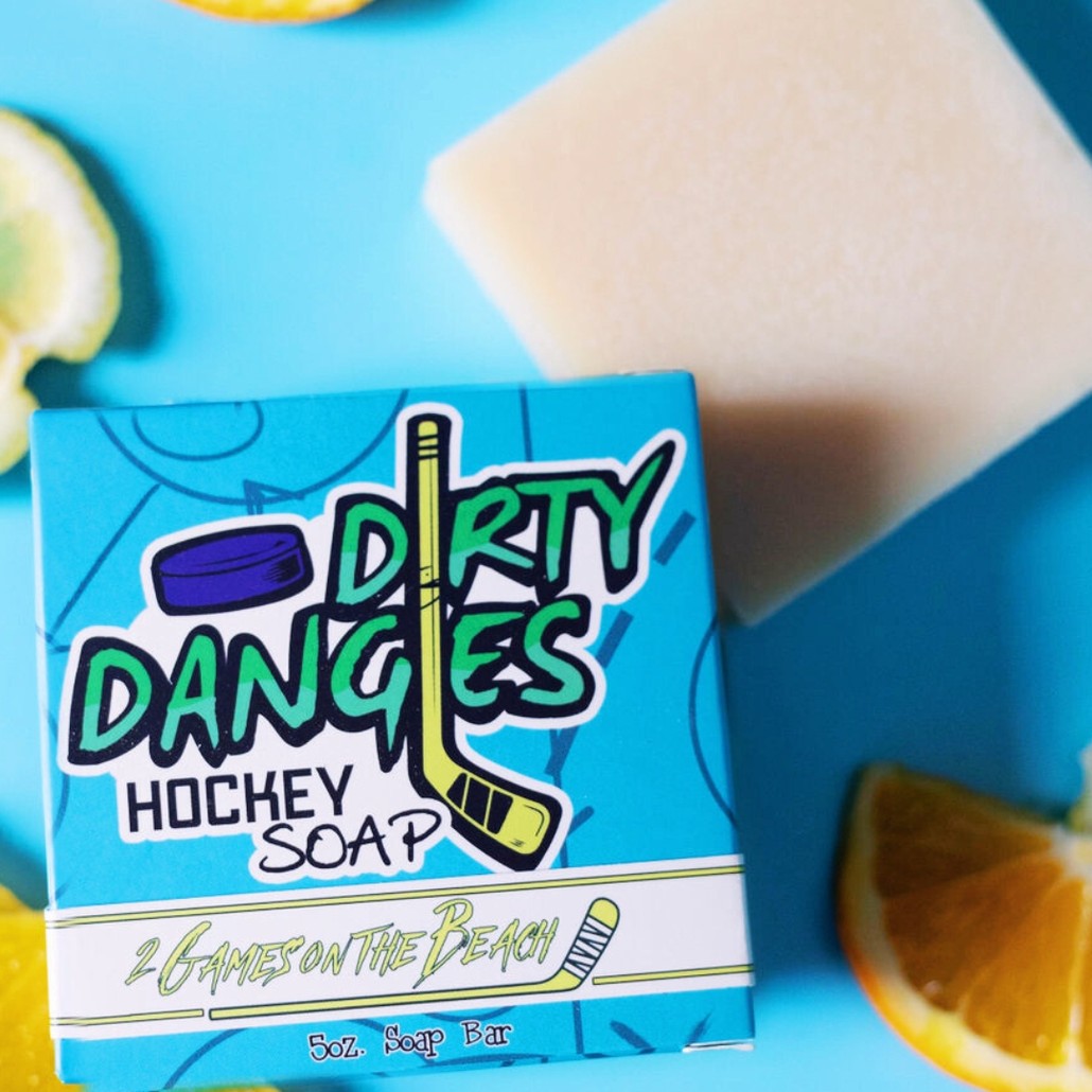 A yellow bar of dirty dangles hockey soap on a blue background with oranges lemons and lavender.