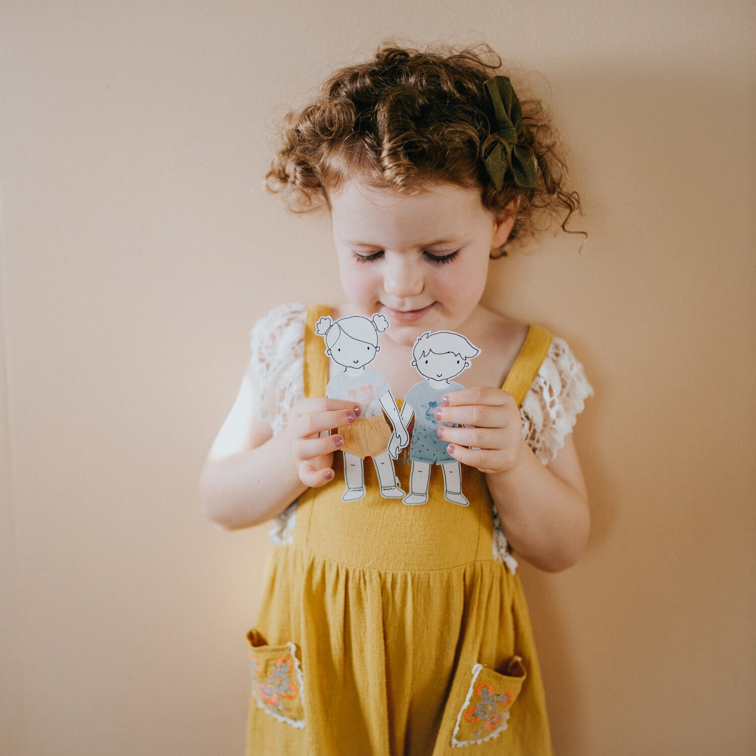 A little girl holds up two paper dolls with paper clothes.