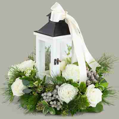 A white wooden lantern surrounded by white roses