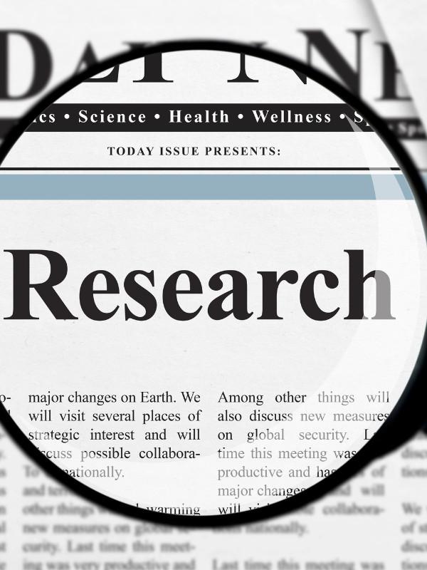 magnifying glass hovering over the word "Research" on a newspaper article