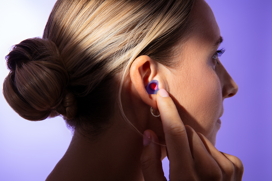 A woman touching her ear containing an earplug used for falling asleep on a plane fast.