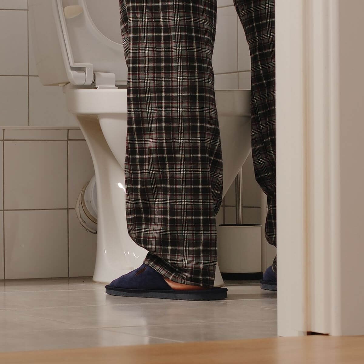 Man wearing slippers and pajamas peeing in a toilet