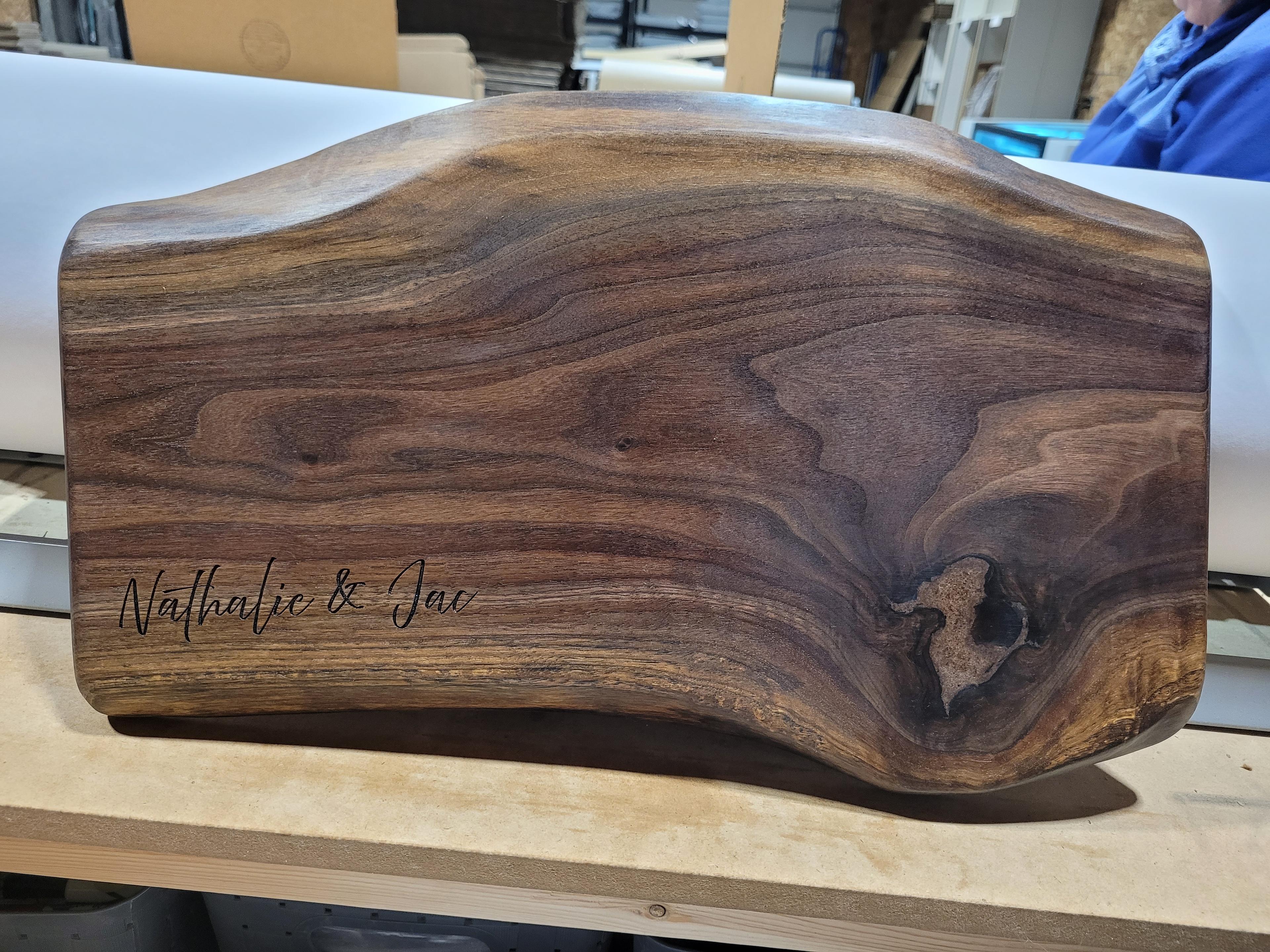 Personalized live edge walnut charcuterie board with custom engraving shown upright in workshop setting