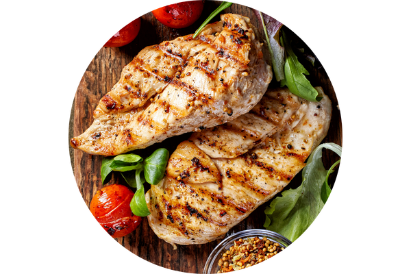 circular image with two chicken breasts on a wooden cutting board surrounded by lettuce, tomatoes, and quinoa