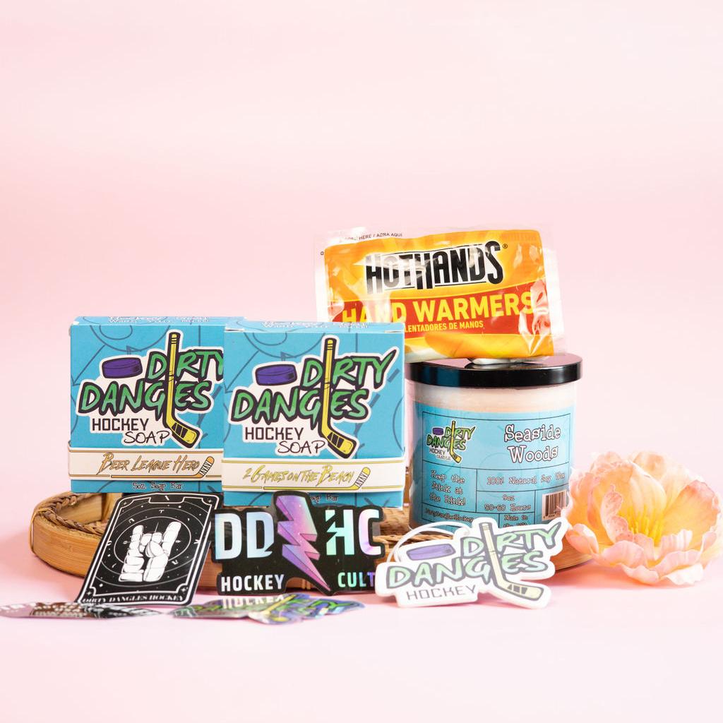 A hockey mom survival kit bundle on a pink background with flowers. 2 soap bars, scented candle, hand warmers, car air freshener and stickers