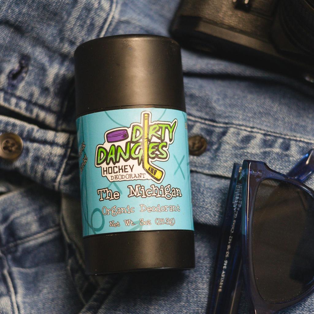 aluminum-free deodorant the michigan scent laying on a pair of jeans with sunglasses and a wallet