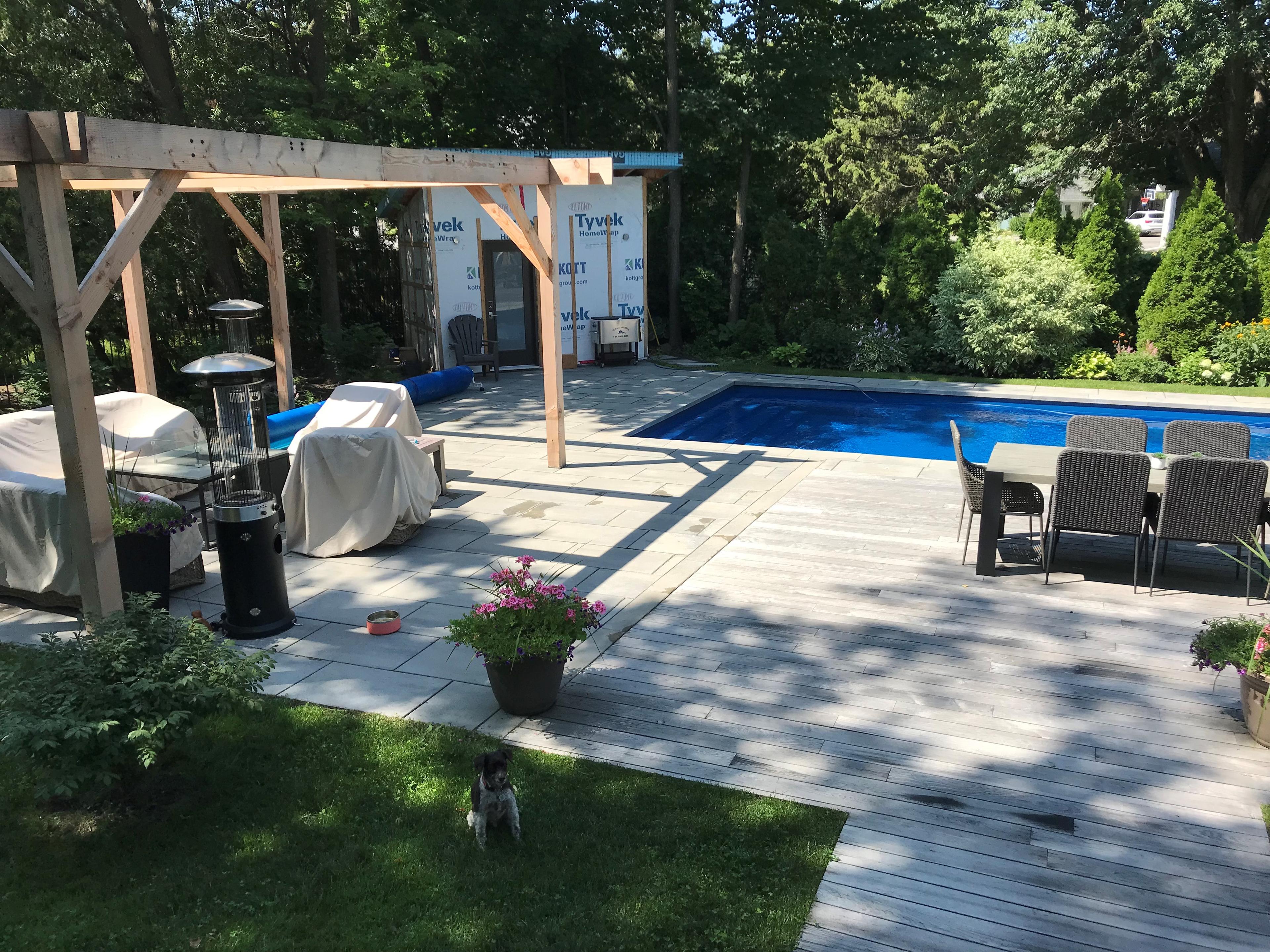 wooden deck butting up against patio stones with an unfinished shed and pergola in the background
